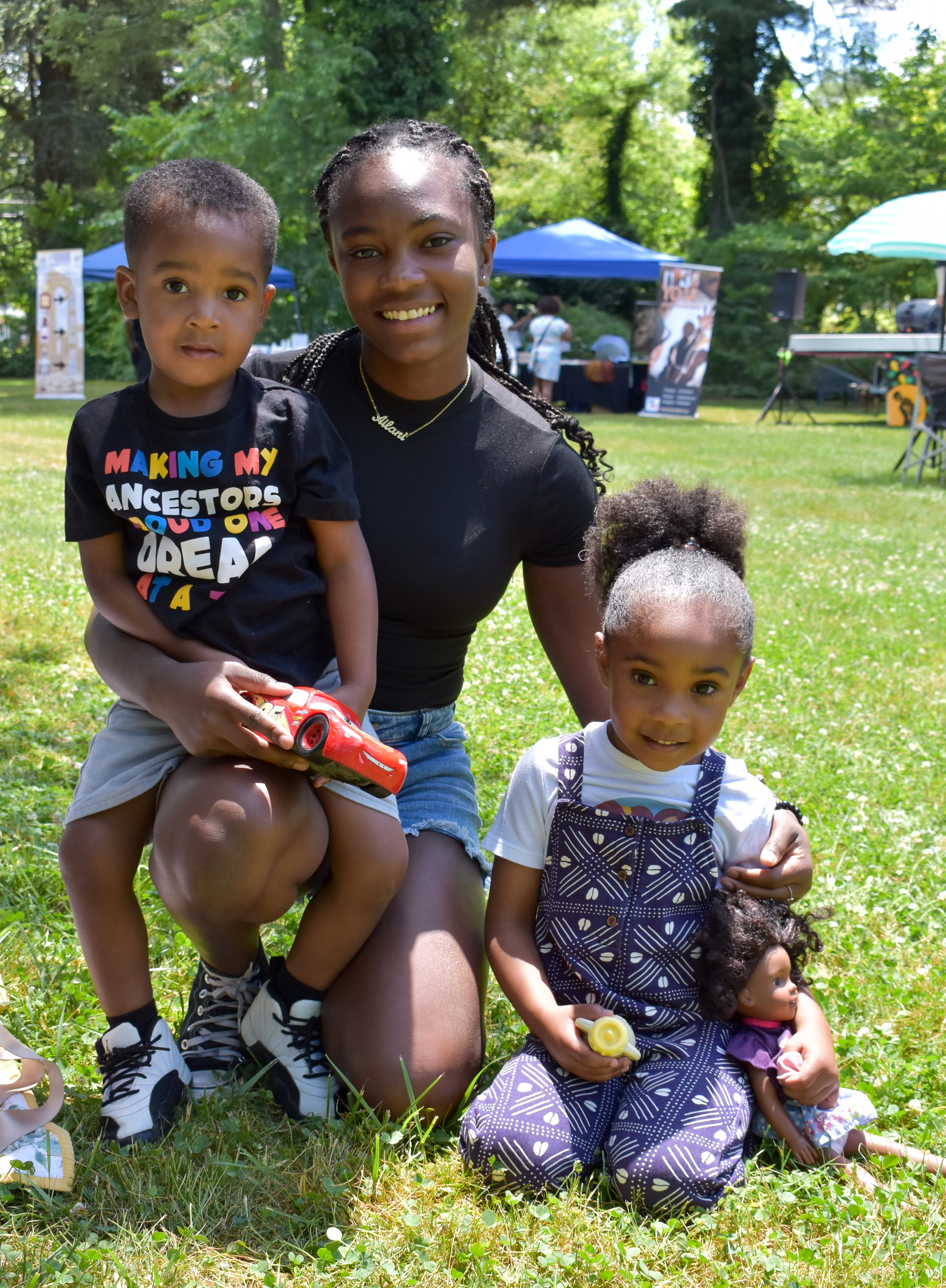 A young woman and two children sitting on grass, enjoying a peaceful moment outdoors at Moorestown Juneteenth
