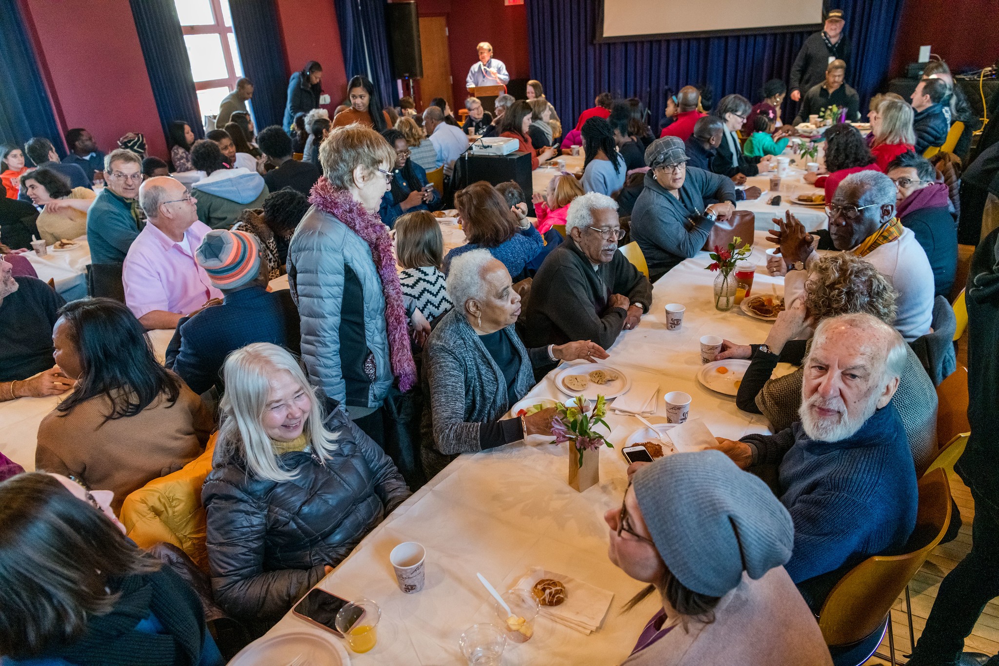 Room full of adults, most of whom are seated at long white tables